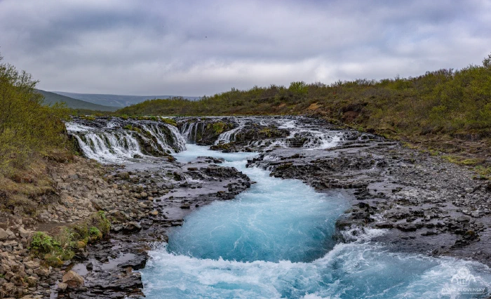Panorama of Bruarfoss, electric-blue glacial water spilling over dark lava ledges