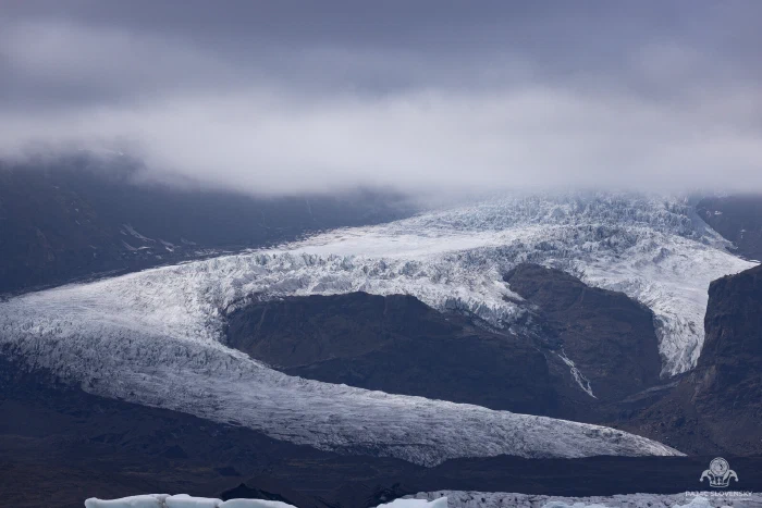 Glacier sweeping around a dark mountain ridge beneath low brooding cloud