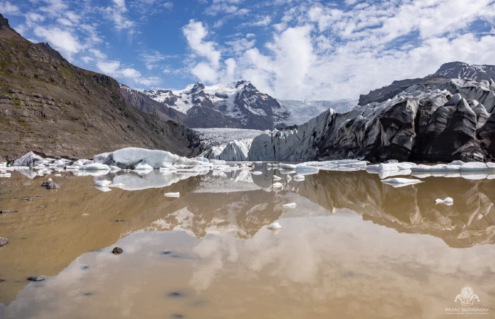 Mirror-calm glacier lagoon reflecting snow-capped peaks and drifting ice