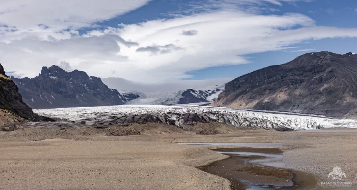 Glacier tongue descending between dark peaks above a braided outwash plain