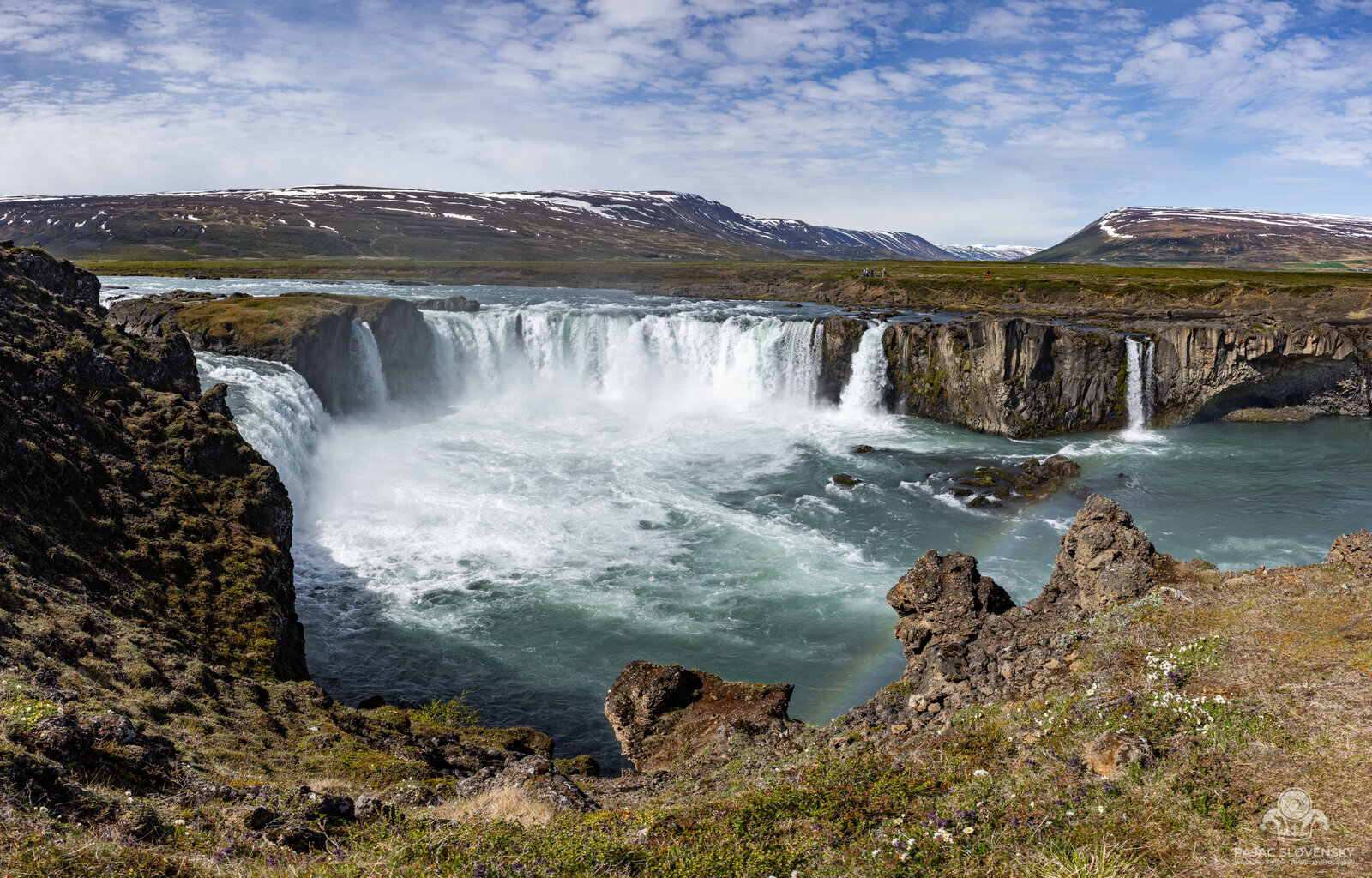 Goðafoss waterfall's full horseshoe thundering beneath snow-streaked hills