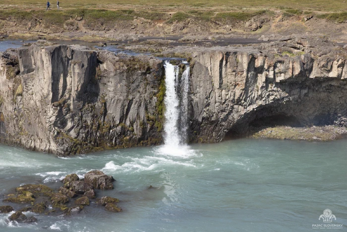 Slender side cascade plunging off basalt cliffs into turquoise water near Godafoss