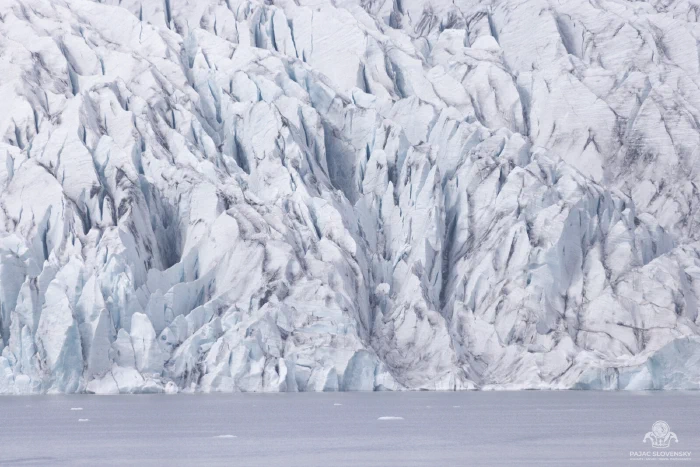 Wall of fractured glacier seracs rising above still grey lagoon water
