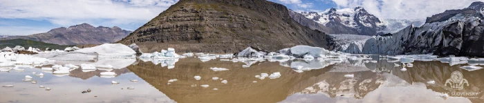 Icebergs mirrored in a silt-brown glacier lagoon beneath barren mountains