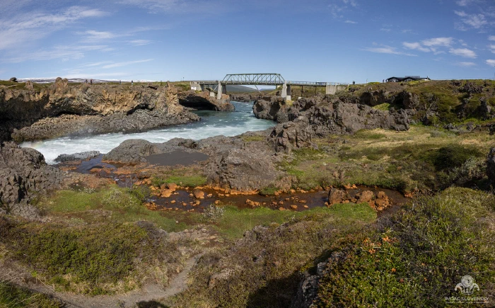 Truss bridge spanning the Skjalfandafljot river amid lava rocks below Godafoss