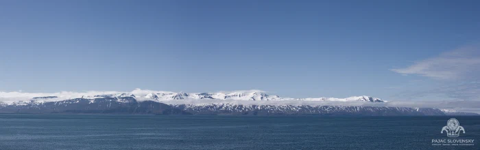 Snow-streaked mountain range across a still northern bay