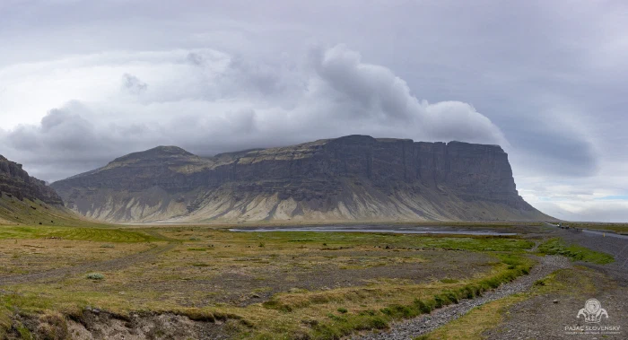 Sheer flat-topped basalt escarpment over green wetland plain, brooding clouds