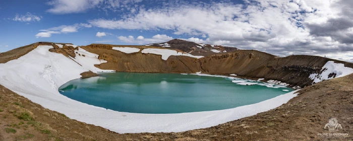 Snow-ringed turquoise lake filling Viti crater at Krafla under drifting clouds