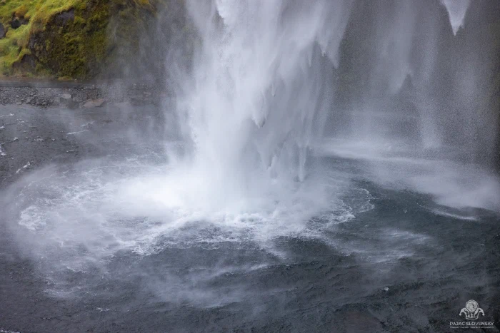 Waterfall column crashing into churning plunge pool, mist and mossy rock