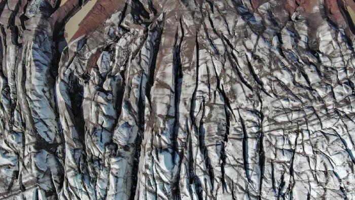 Dark ash-covered glacier fissures radiating downward, hints of rust rock