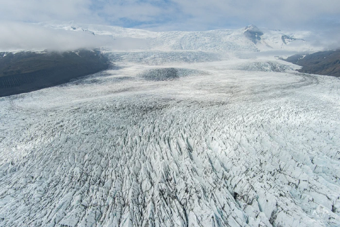 Swirls of dark volcanic ash marbling a vast white glacier expanse