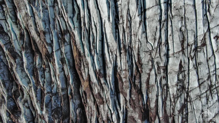 Aerial of blue glacier ice furrowed and veined with volcanic ash