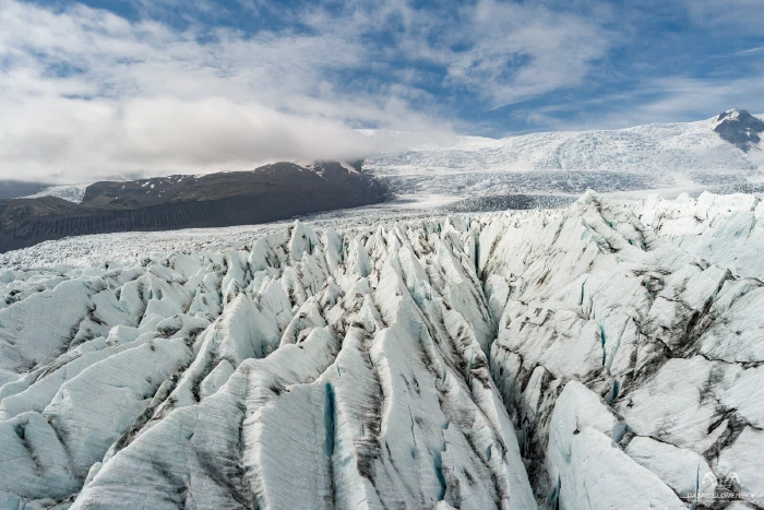 Jagged blue-white glacier crevasse pinnacles with ash streaks under blue sky