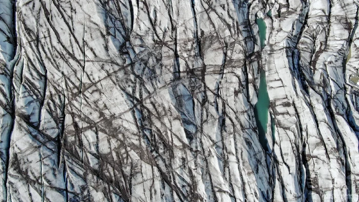 White glacier crisscrossed by dark crevasses with emerald meltwater pool