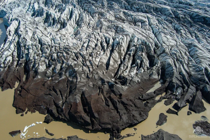 Crevassed white glacier front above dark moraine ice and muddy water