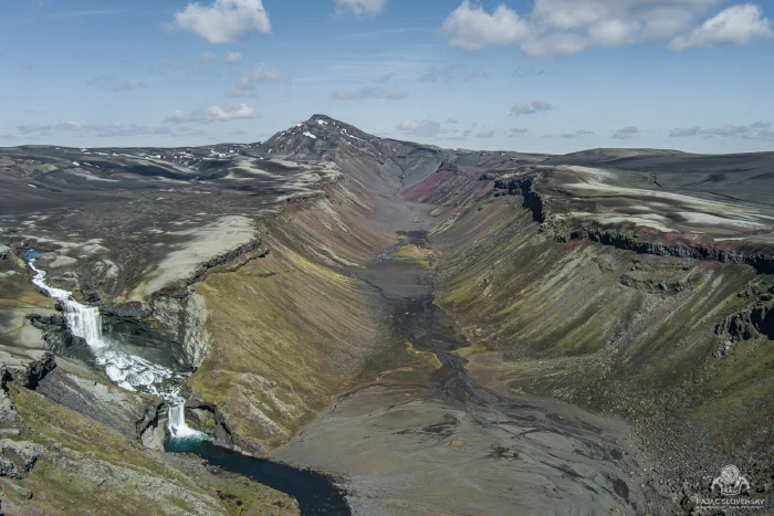 Eldgja canyon panorama: red-streaked walls, twin falls, braided black floor
