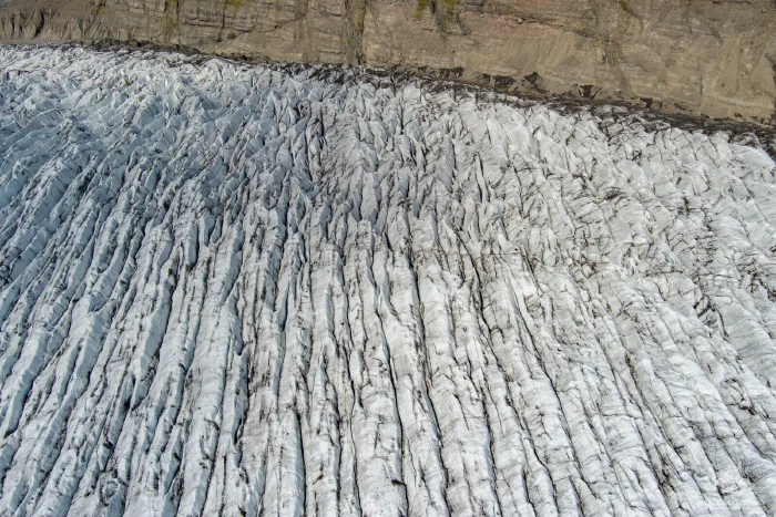 Aerial of parallel glacier crevasse ridges meeting brown moraine wall