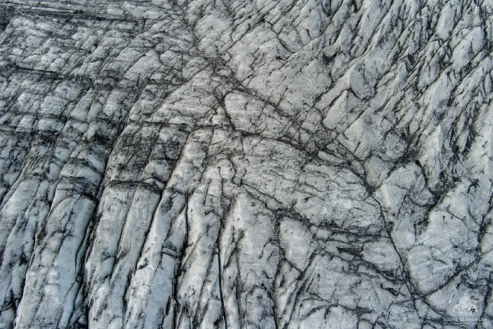 Top-down glacier ice, crisscrossing crevasses veined with black ash