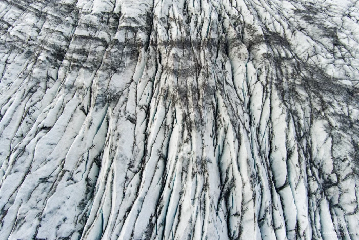 Parallel glacier crevasses streaked with ash, abstract vertical furrows