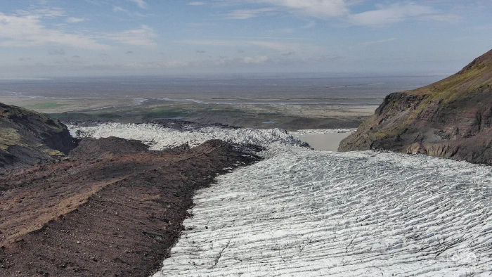 Striped glacier ice and brown moraine descending toward flat coastal plain