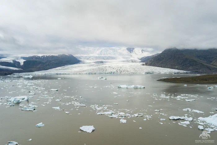 Glacier tongue descending to an iceberg-strewn grey lagoon under low cloud