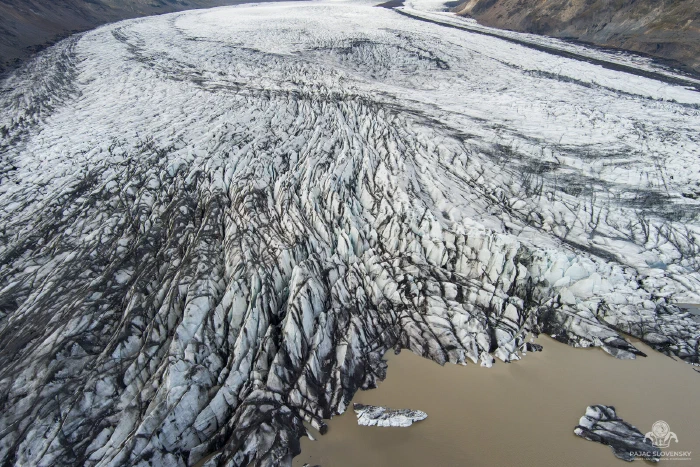 Crevassed glacier tongue fanning into a brown meltwater lagoon with icebergs