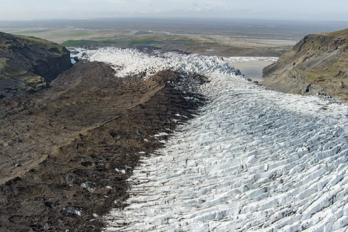 Aerial of a glacier tongue with dark moraine ridge descending to a lagoon