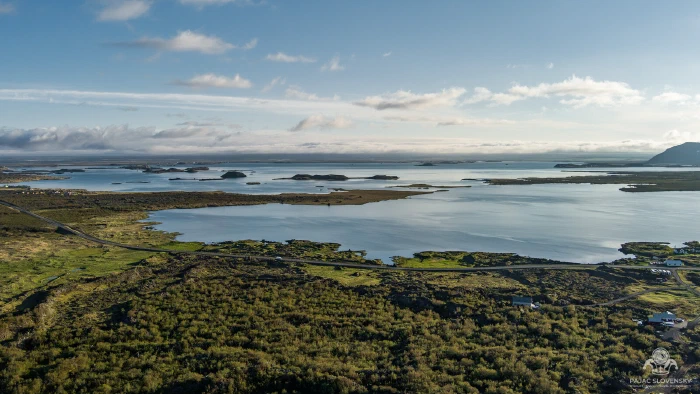 Island-dotted blue lake beyond sunlit green scrubland under low cloud bank