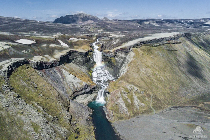 Ófærufoss from above with a rainbow arcing over the falls and turquoise pool