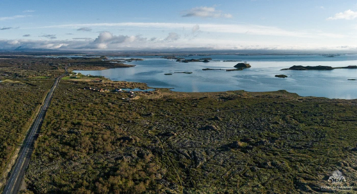 Straight road slicing mossy lava field toward island-studded blue lake