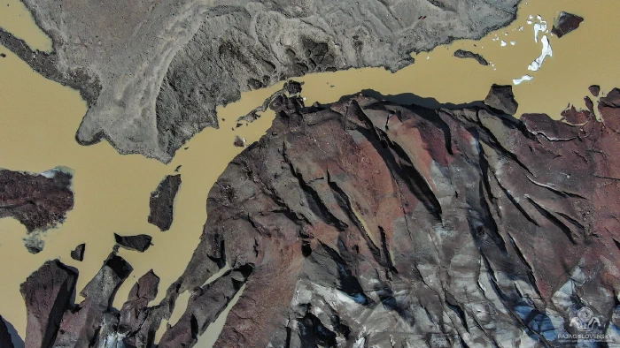 Top-down view of rust-red debris-covered ice meeting khaki glacial meltwater