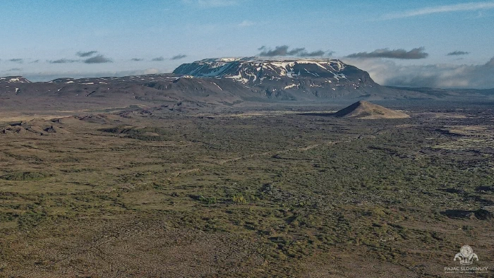 Snow-streaked table mountain rising above a vast green lava plain