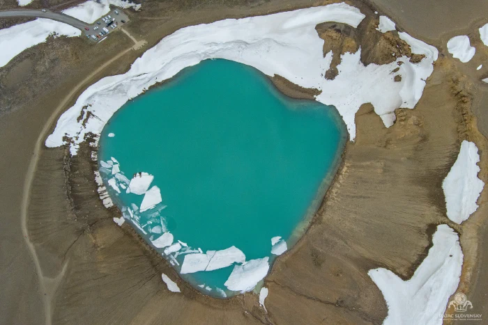 Turquoise crater lake with drifting white ice slabs, top-down aerial