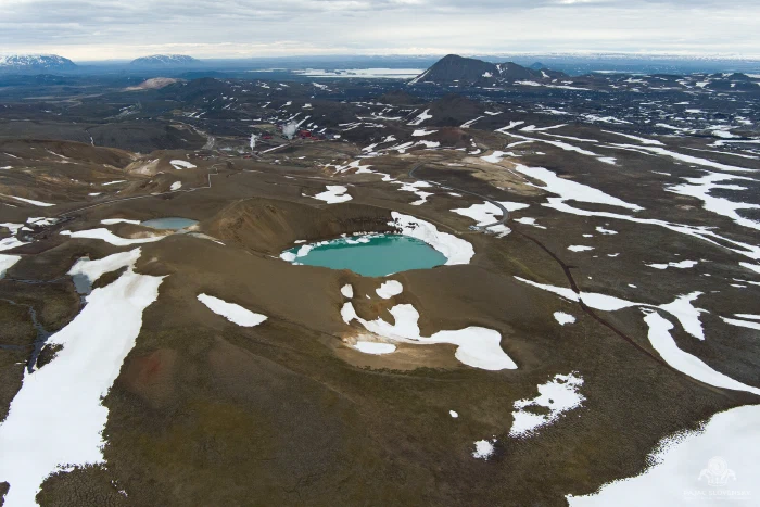 Turquoise crater lake ringed by snow patches on brown volcanic terrain