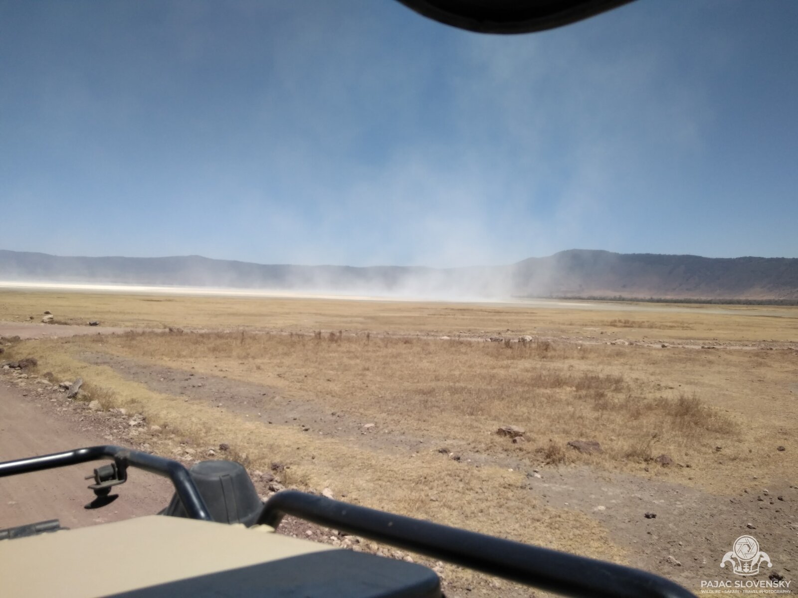 Wind lifting soda dust across the Ngorongoro crater floor, seen over the truck's roof rack