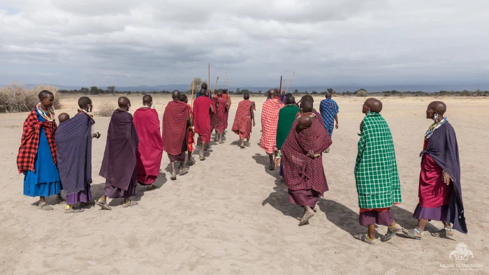 Villagers in colorful shukas walking away across a dry plain
