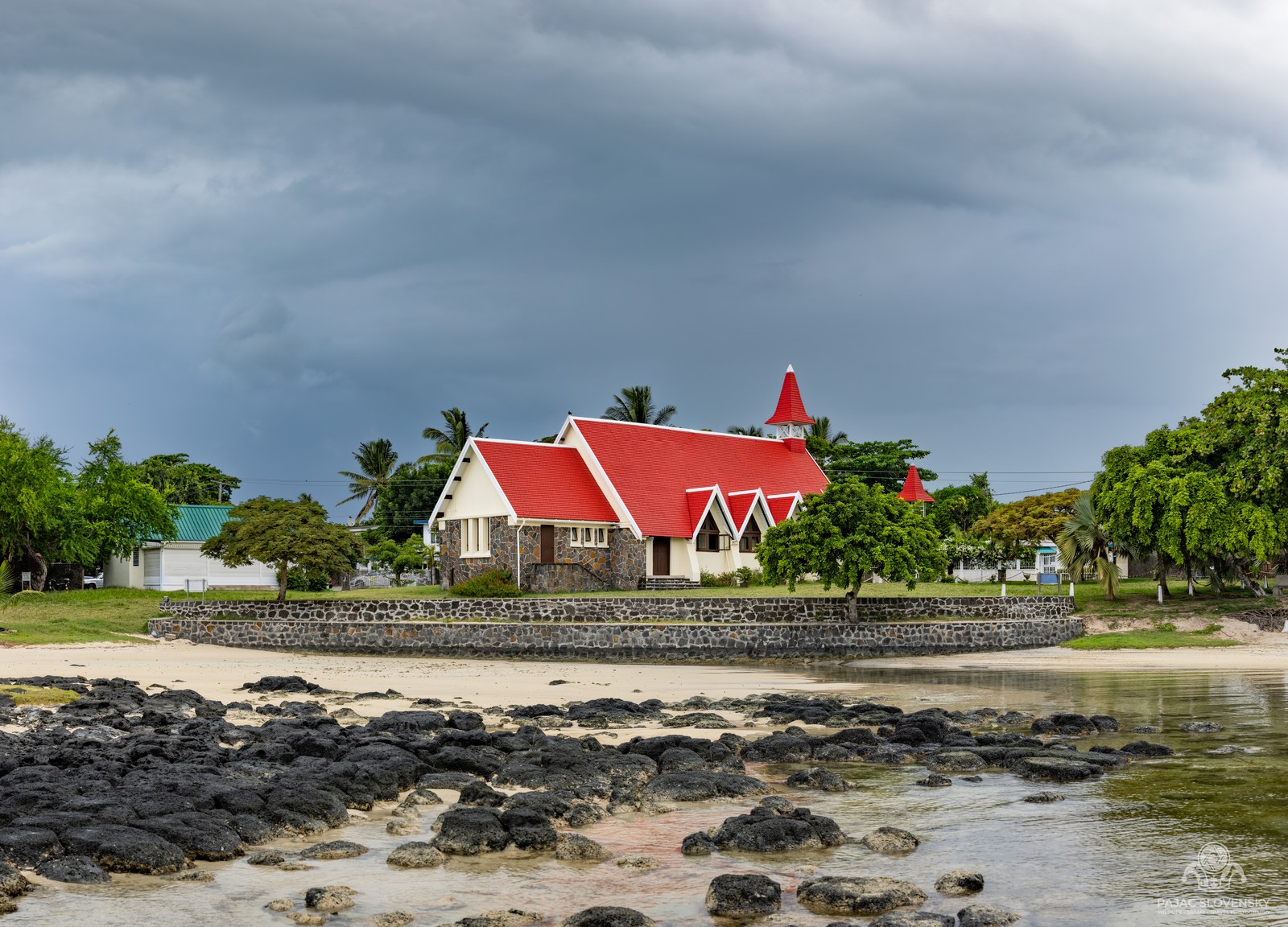Red-roofed church of Cap Malheureux behind lava rocks under storm clouds