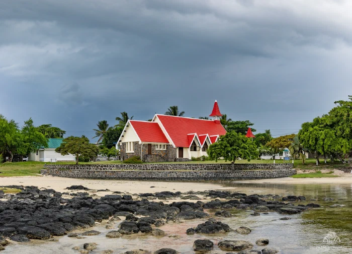 Red-roofed church of Cap Malheureux behind lava rocks under storm clouds