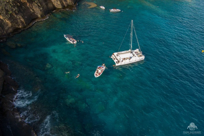Aerial of a catamaran and snorkelers anchored below Coin de Mire's cliffs