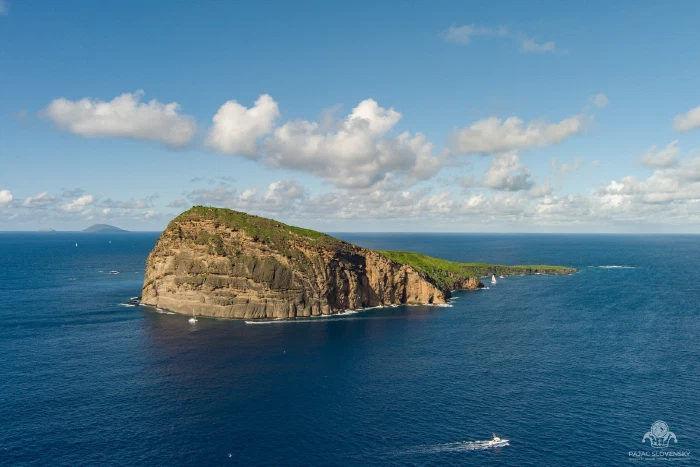 The sheer basalt cliff face of Coin de Mire above a passing boat