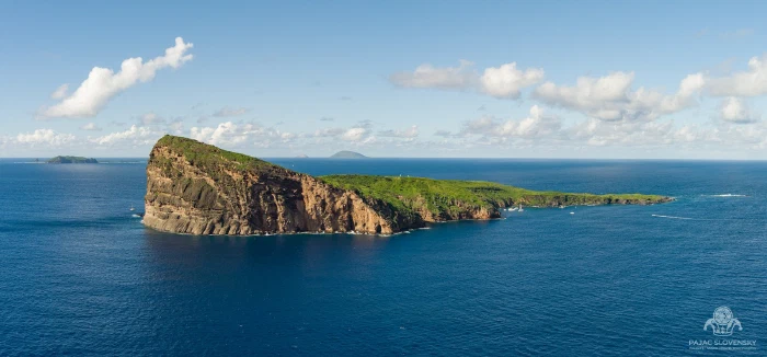 Panorama of Coin de Mire island's tilted wedge rising from deep blue sea
